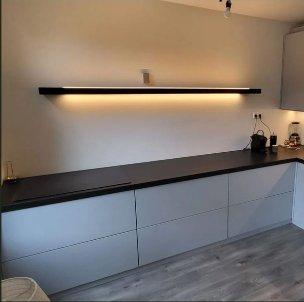 Moderne keuken met grijze kasten, zwart aanrechtblad en een lange zwarte lamp.