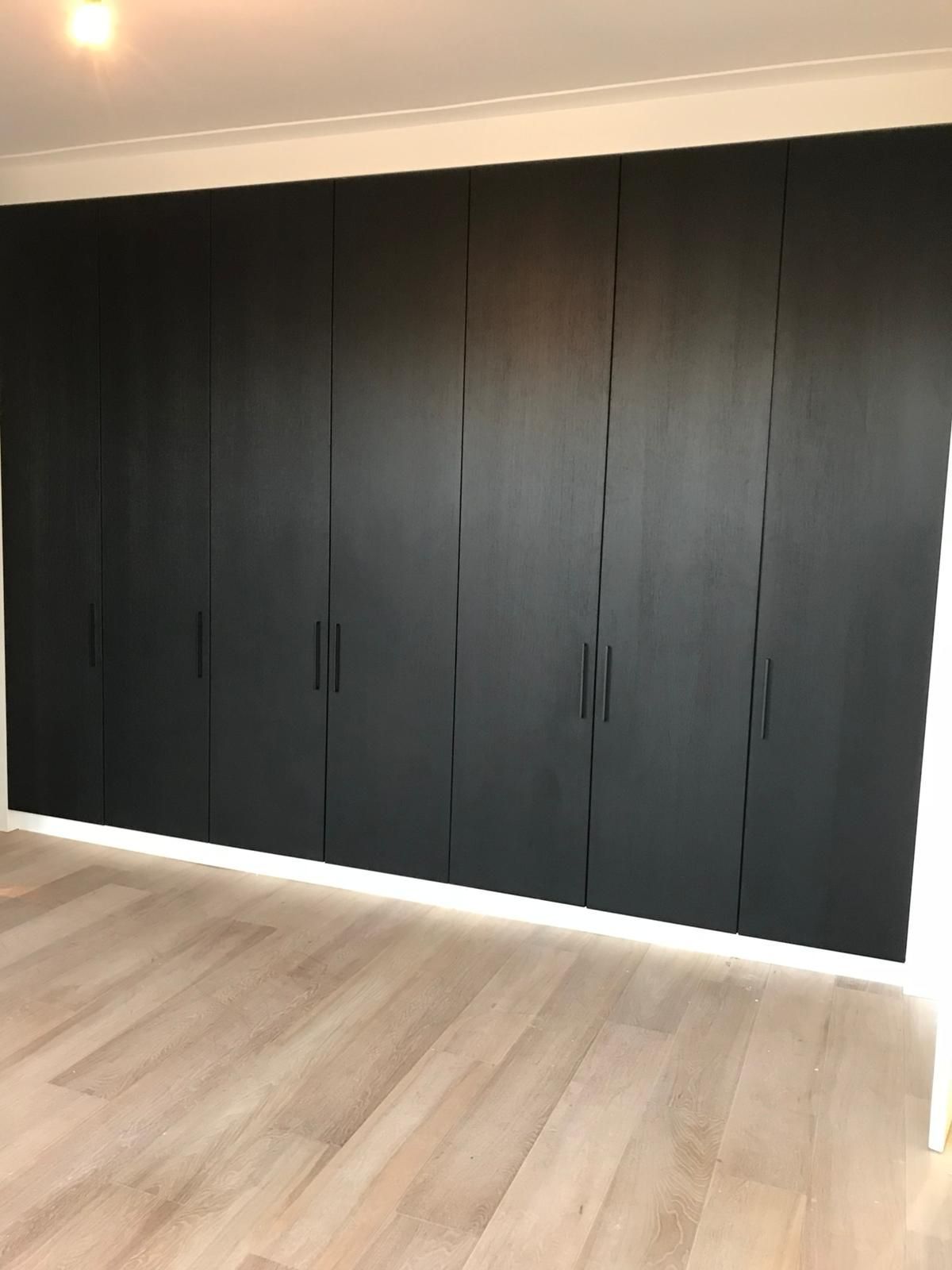 Zwarte kledingkastdeuren tegen een wit plafond en een lichte houten vloer.