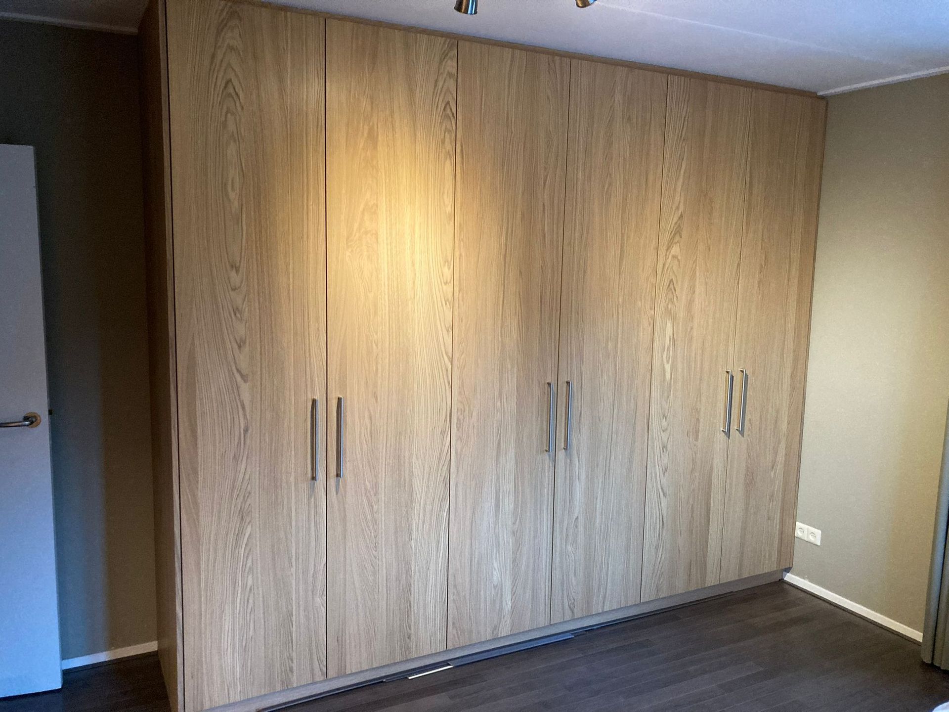 Grote houten kast met meerdere deuren en donkere metalen handgrepen.