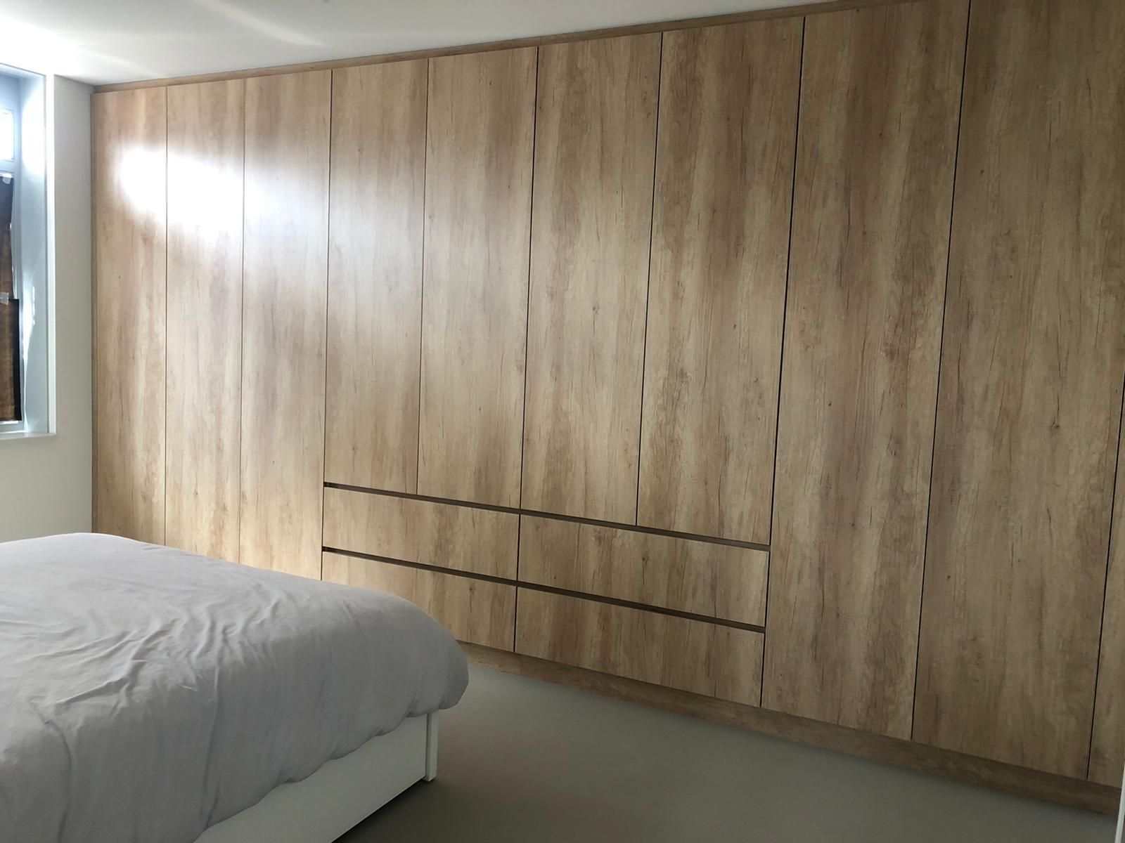Slaapkamer met kastdeuren met lichte houtnerf en een grijs bed.