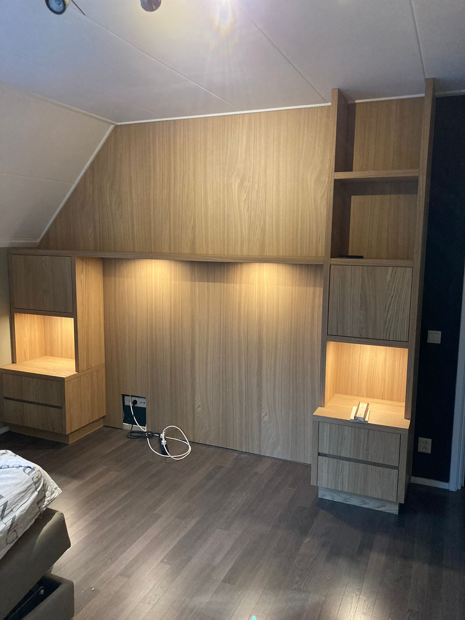 Ingebouwde houten slaapkamerkast met planken en lades. Hardhouten vloer en schuin plafond.