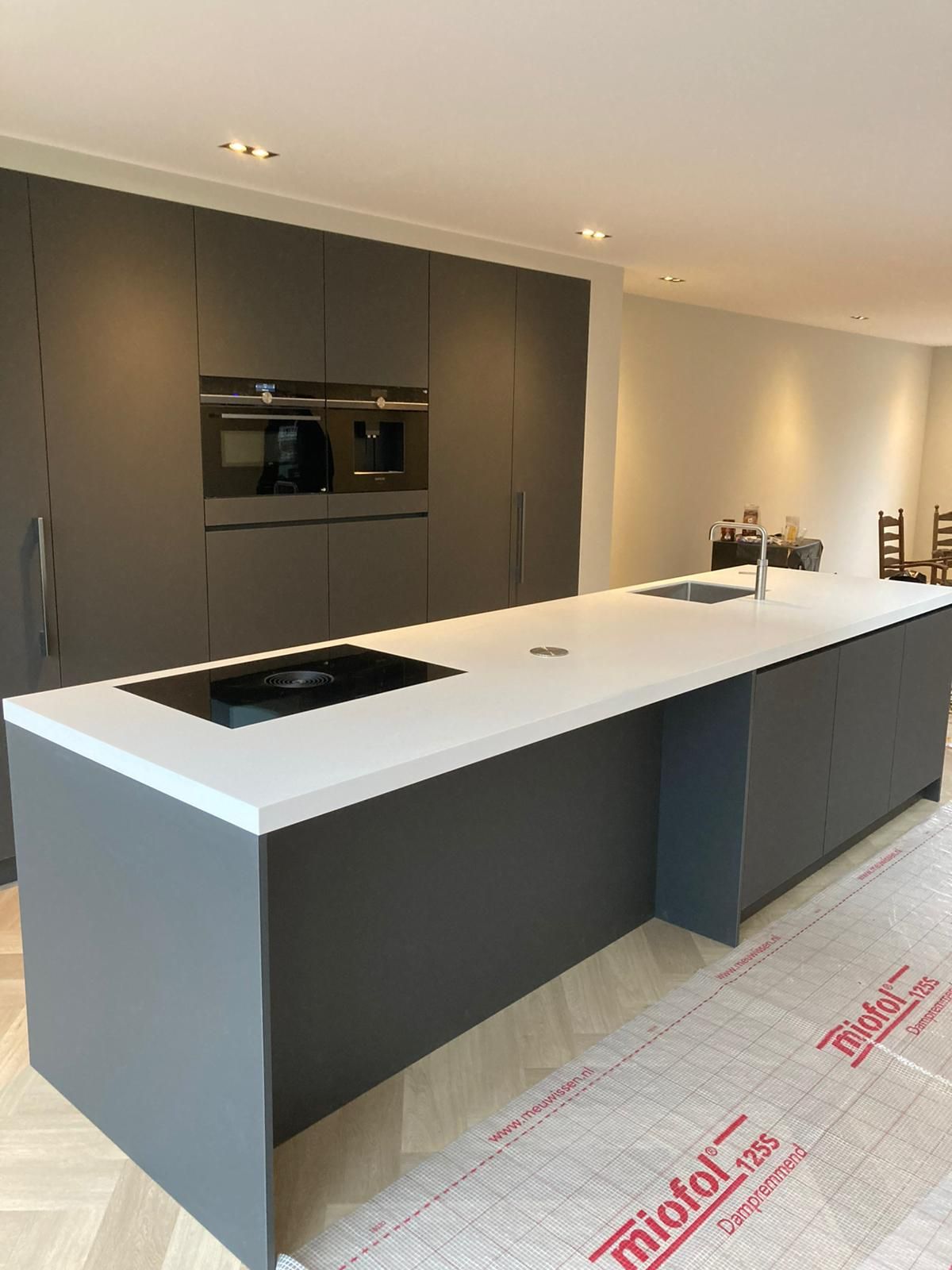 Moderne keuken met grijze kasten, wit kookeiland en inbouwapparatuur.