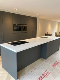 Moderne grijze keuken met groot kookeiland, ingebouwde kookplaat en oven, onderbouw met vloerbescherming.