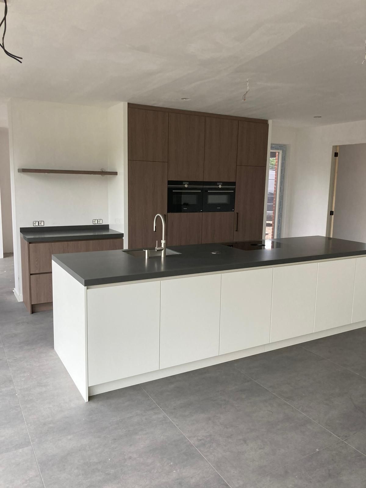 Moderne keuken met wit kookeiland, donkere werkbladen en bruine kasten. Grijze tegelvloer.