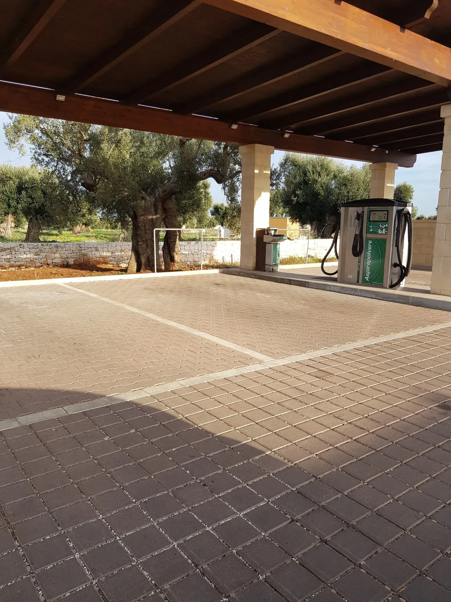 Parcheggio coperto con pavimentazione in mattoni, alberi e stazione di lavaggio auto.