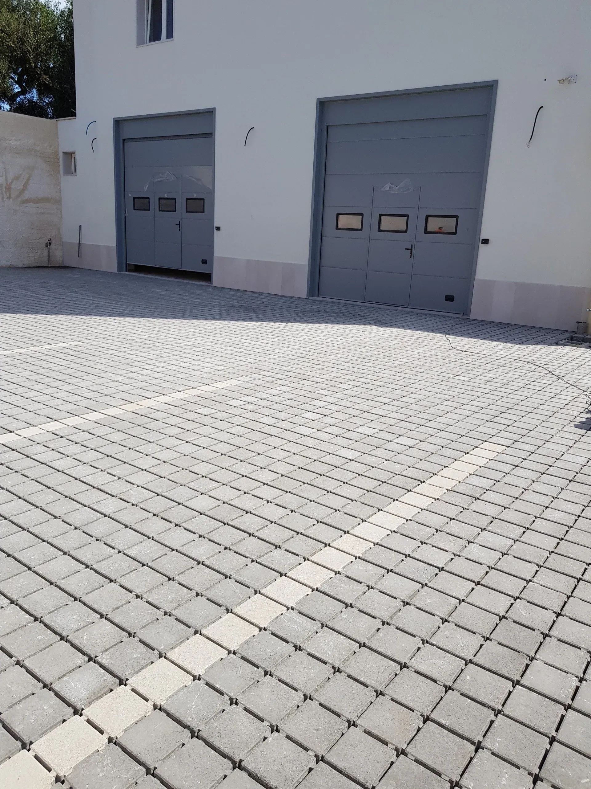 Due portoni da garage grigi su un edificio bianco, area pavimentata con mattoni grigi.