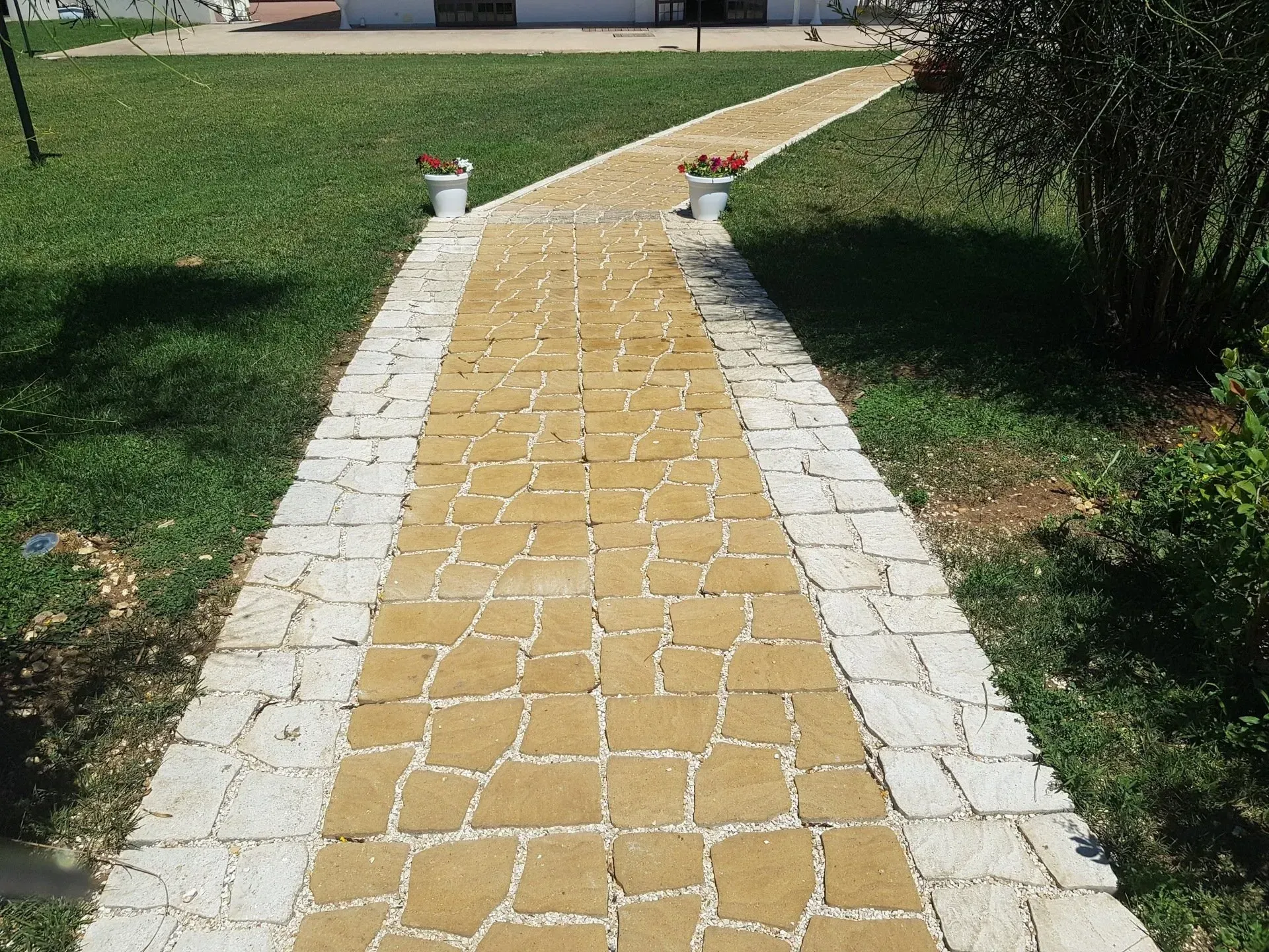 Sentiero in pietra con centro giallo e bordo grigio chiaro, che conduce verso un edificio.
