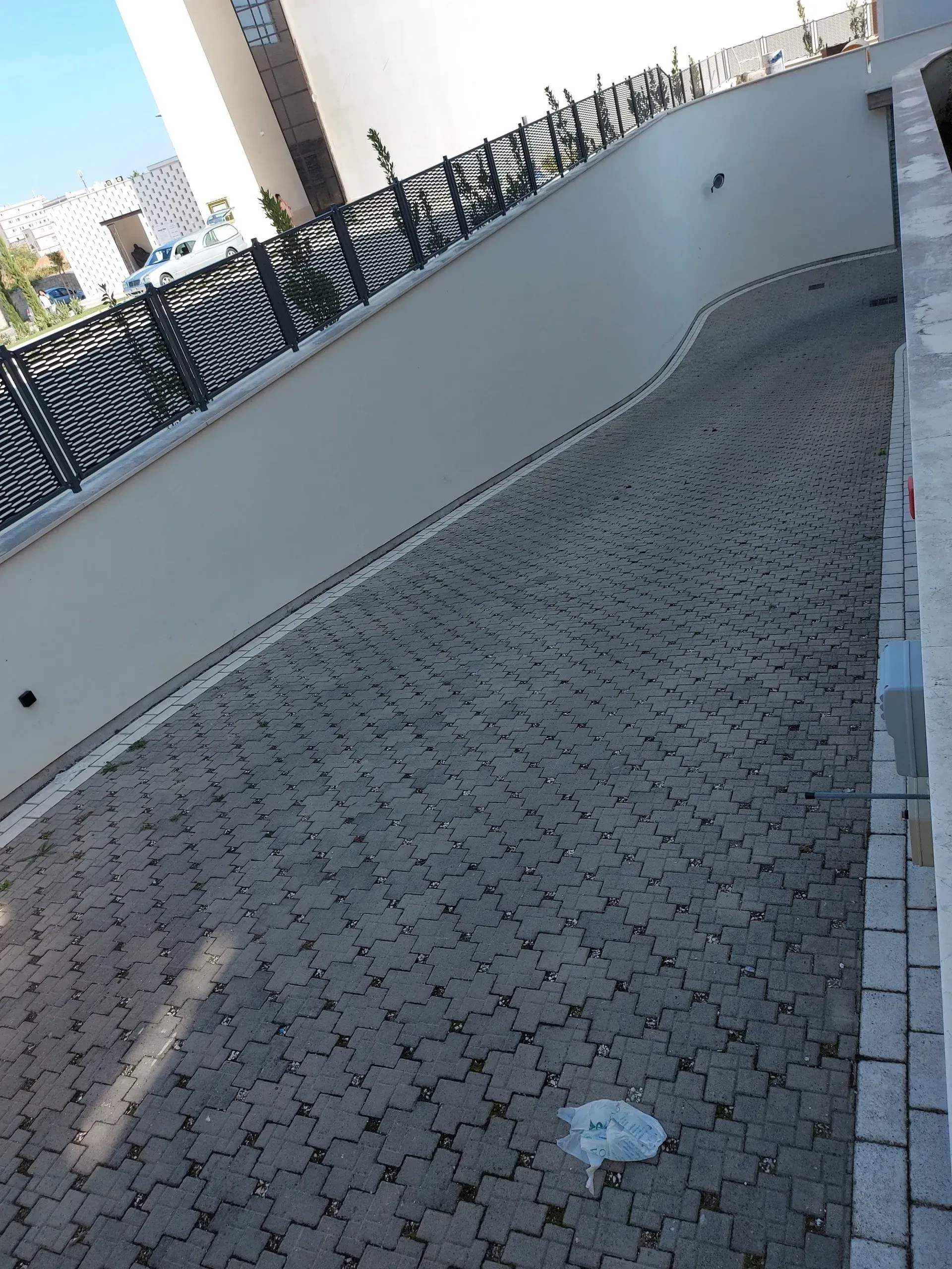 Vialetto d'asfalto in salita, fiancheggiato da un muro bianco e da una recinzione nera.
