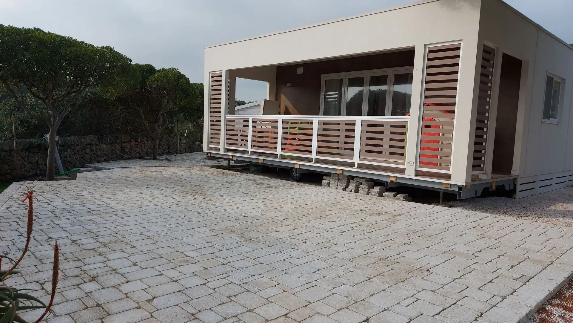 Un piccolo edificio bianco con un portico in legno su un'area pavimentata.