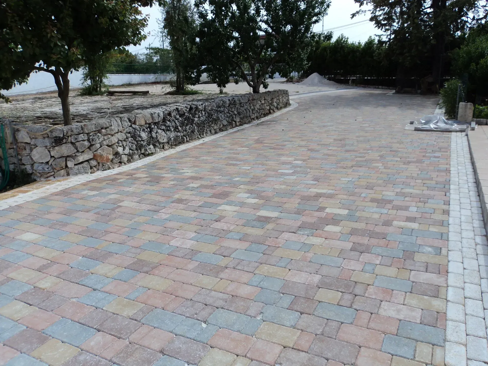Vialetto in mattoni con muro in pietra e piccoli alberi.