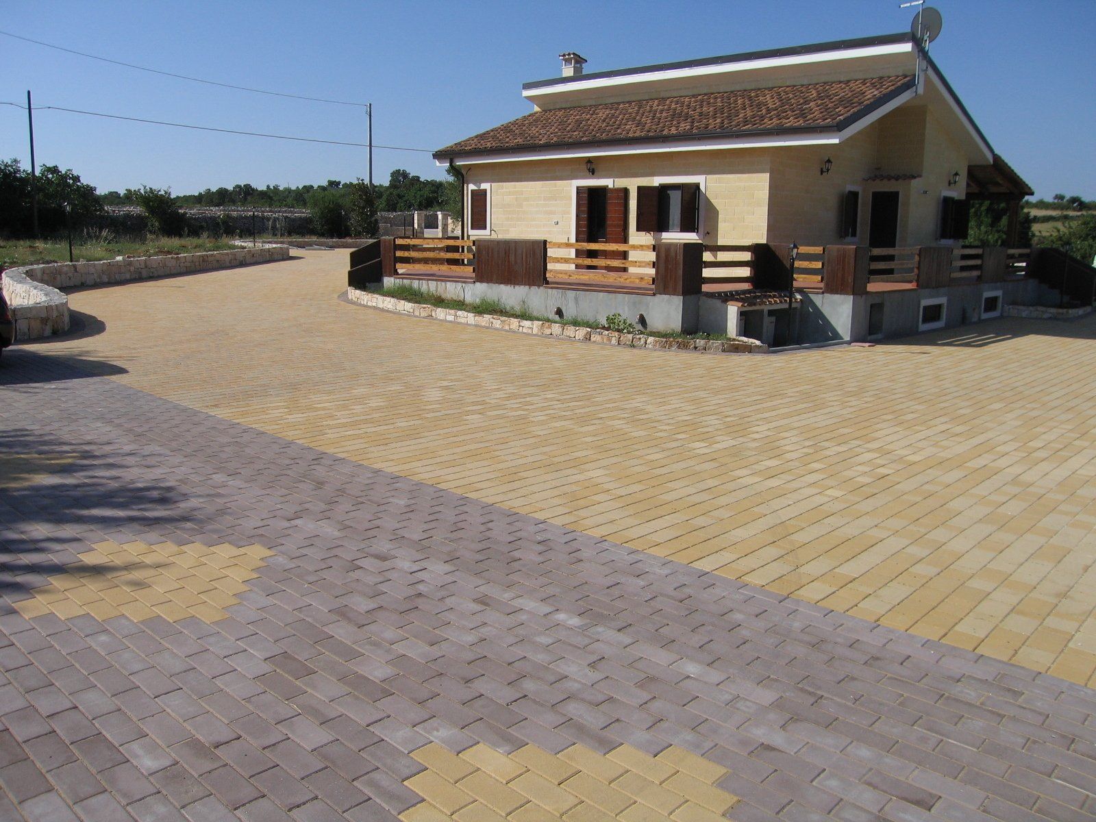 Casa con facciata gialla e tetto marrone, situata su un vialetto di mattoni decorati.