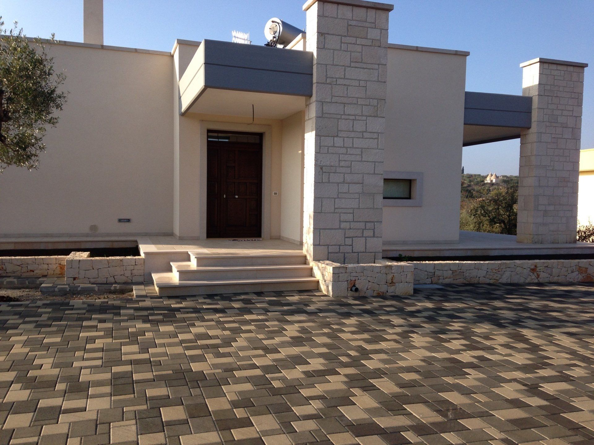 Esterno di una casa moderna con dettagli in pietra, porta scura e ingresso pavimentato.