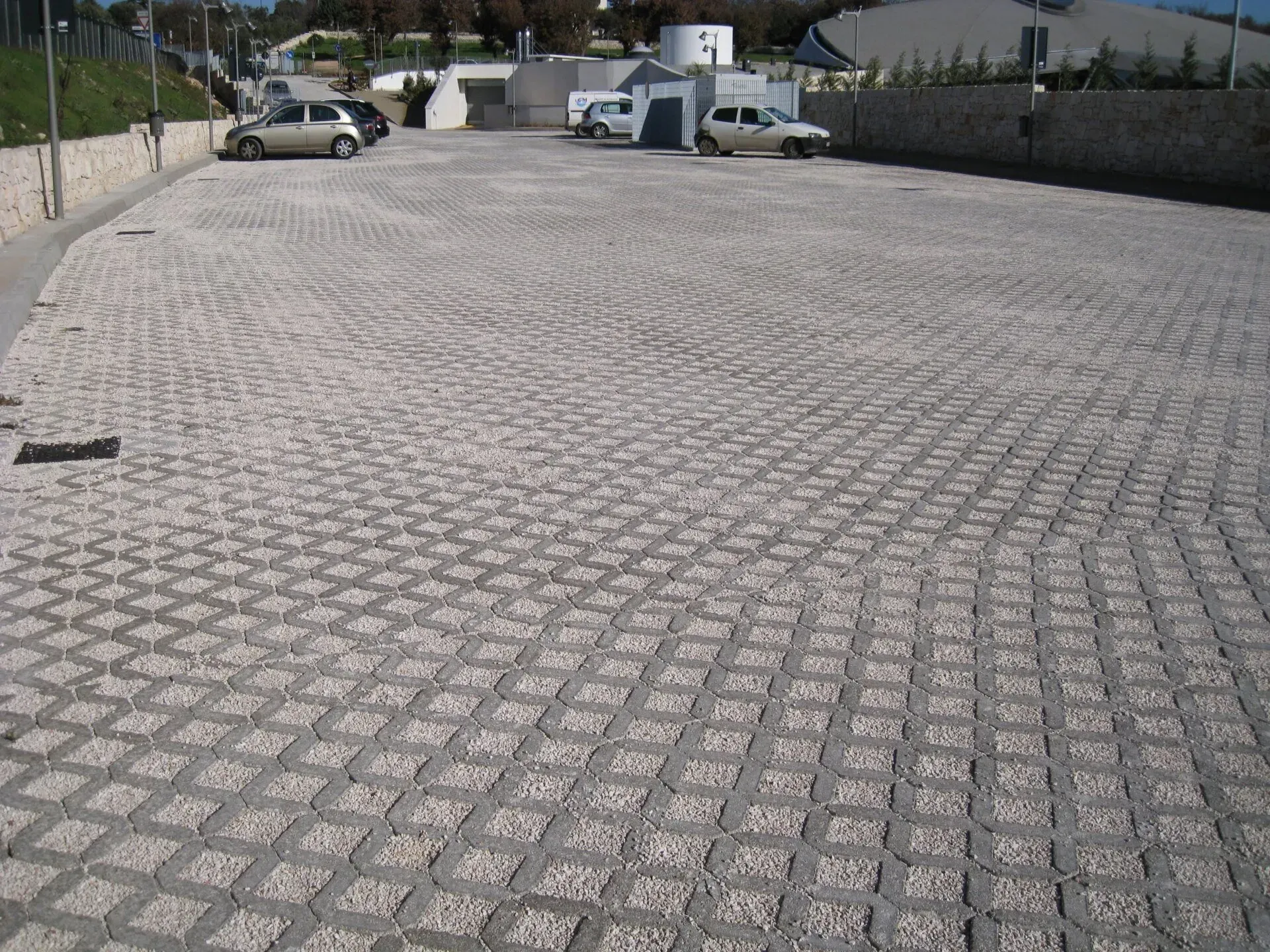 Parcheggio pavimentato con blocchi di cemento autobloccanti; diverse auto parcheggiate.