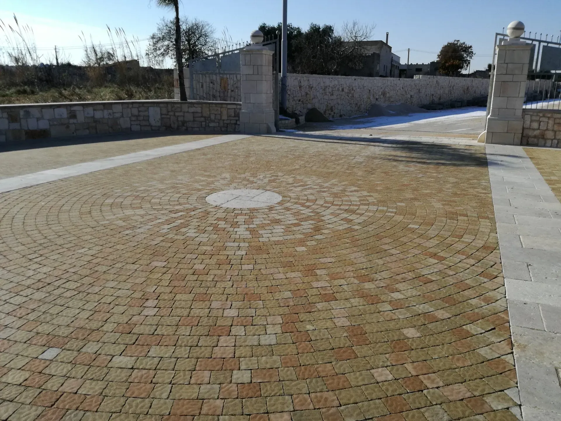 Vialetto circolare in mattoni con pilastri e muro in pietra.