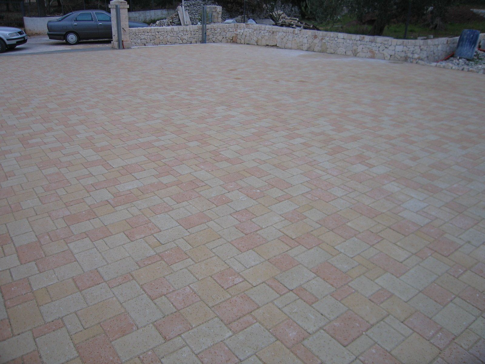 Vialetto pavimentato in mattoni color marrone chiaro e rosa, delimitato da un muro in pietra.