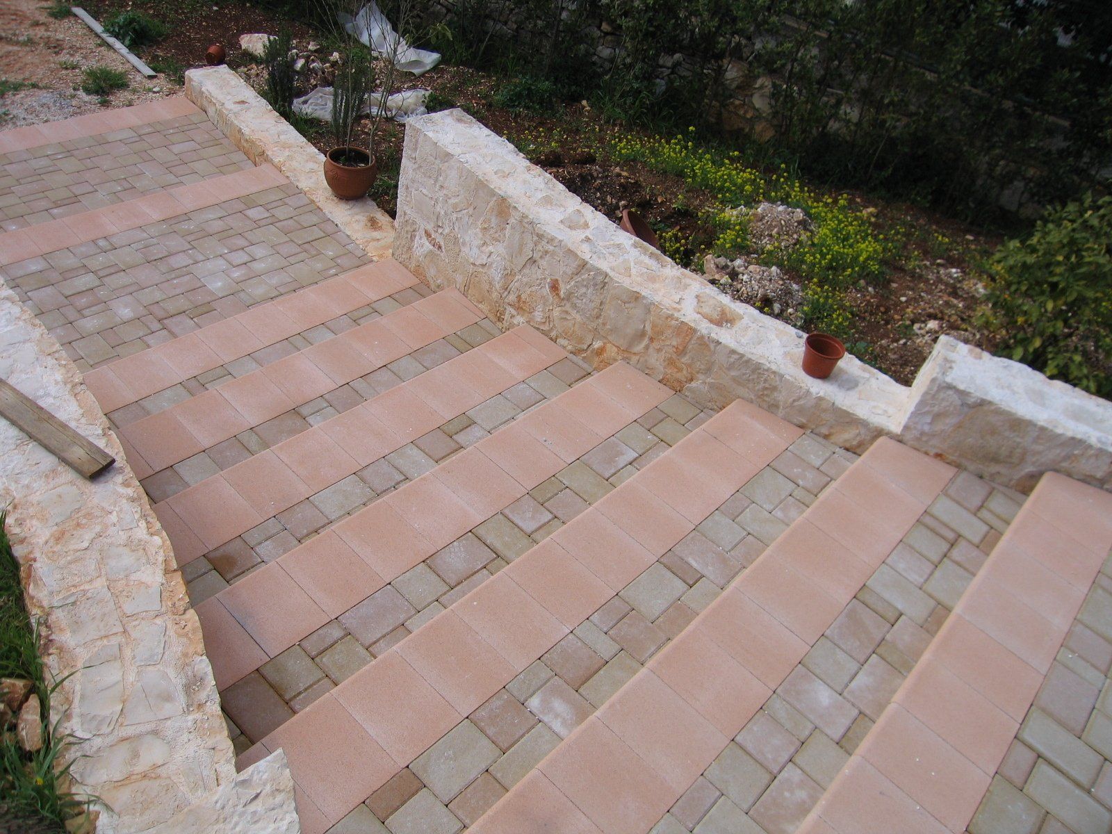Gradini in pietra che scendono, decorati con mattoni, delimitati da muri in pietra e vegetazione.