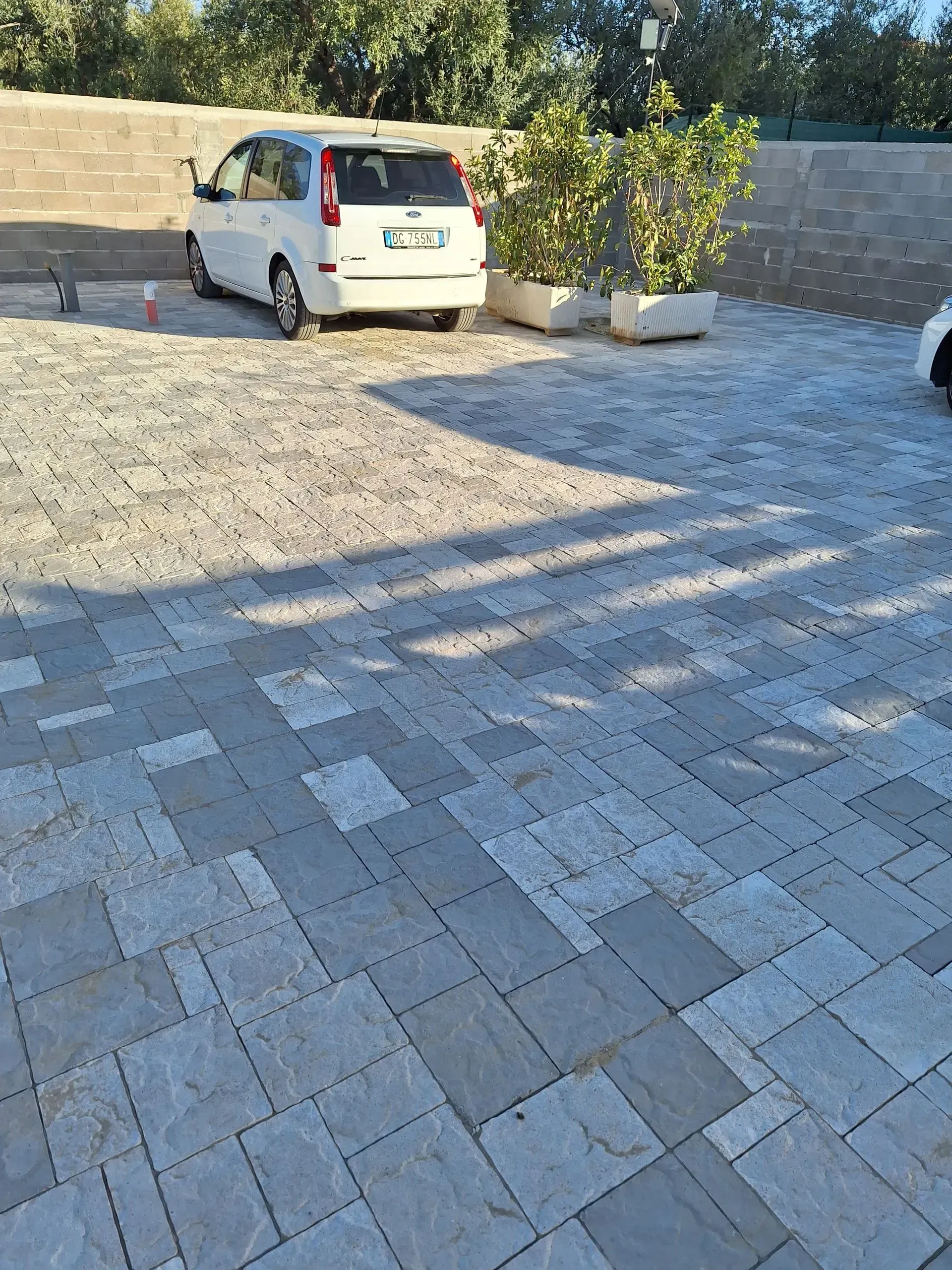 Auto parcheggiata in un parcheggio asfaltato; ombre proiettate da una struttura soprastante.