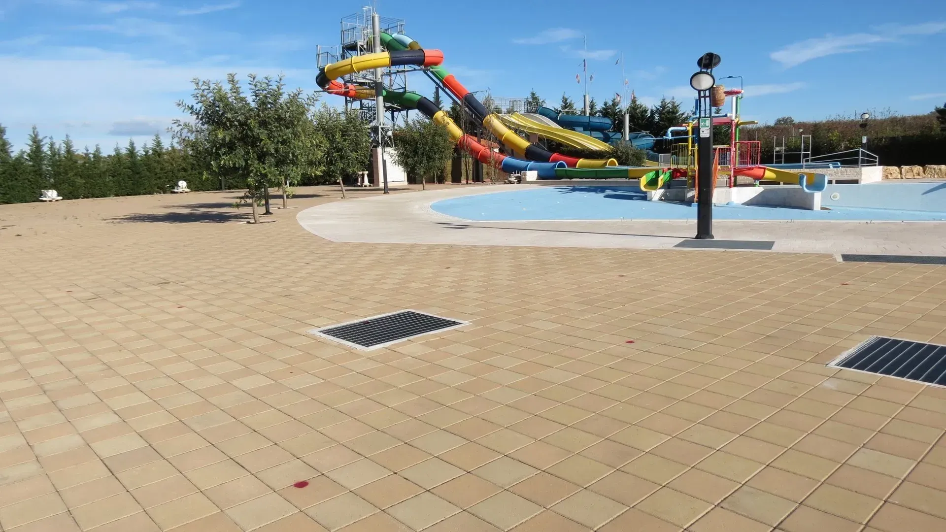 Un parco acquatico con scivoli colorati, una piscina blu e una pavimentazione in mattoni color cuoio nelle giornate di sole.