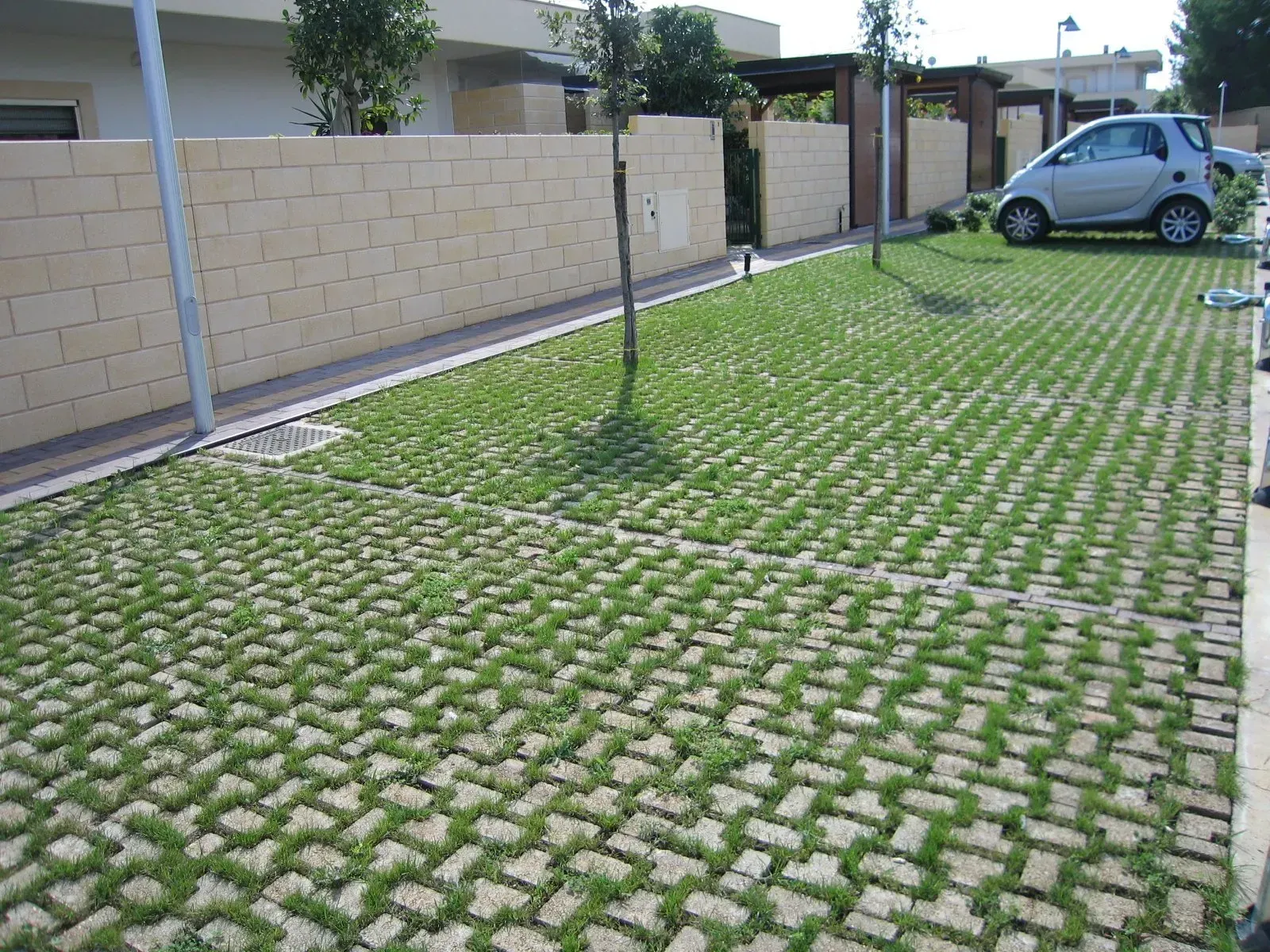 Parcheggio erboso con una piccola auto e un muro di pietra.