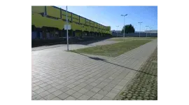 Un'area pavimentata con uno spartitraffico erboso e un edificio sullo sfondo in una giornata di sole.