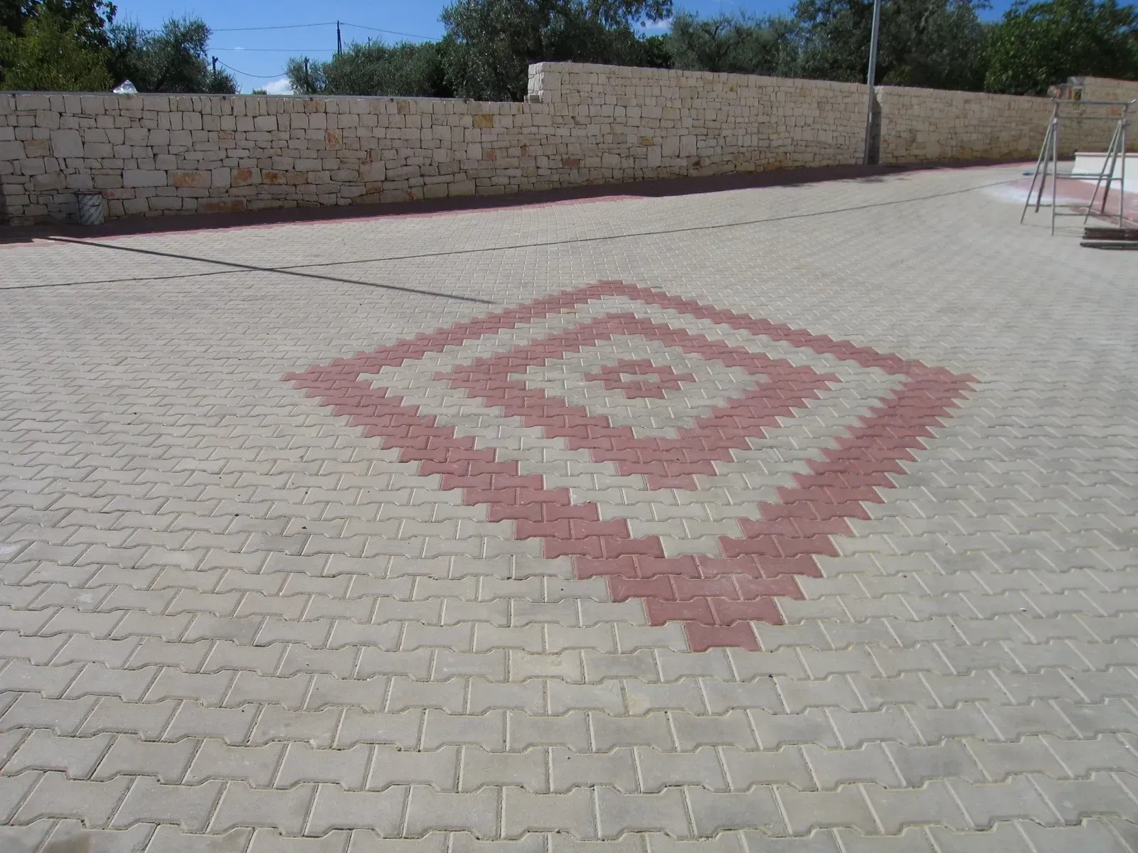 Area pavimentata con mattoni chiari e motivo a rombi rossi. Muro di pietra sullo sfondo.