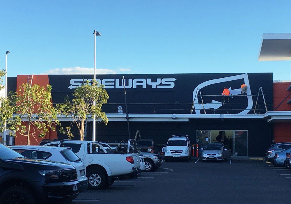 Side Ways Hand Painted Signage Outlet with Two Men Painting on a Logo — Hand Painted Signs in Tweed Heads South, NSW