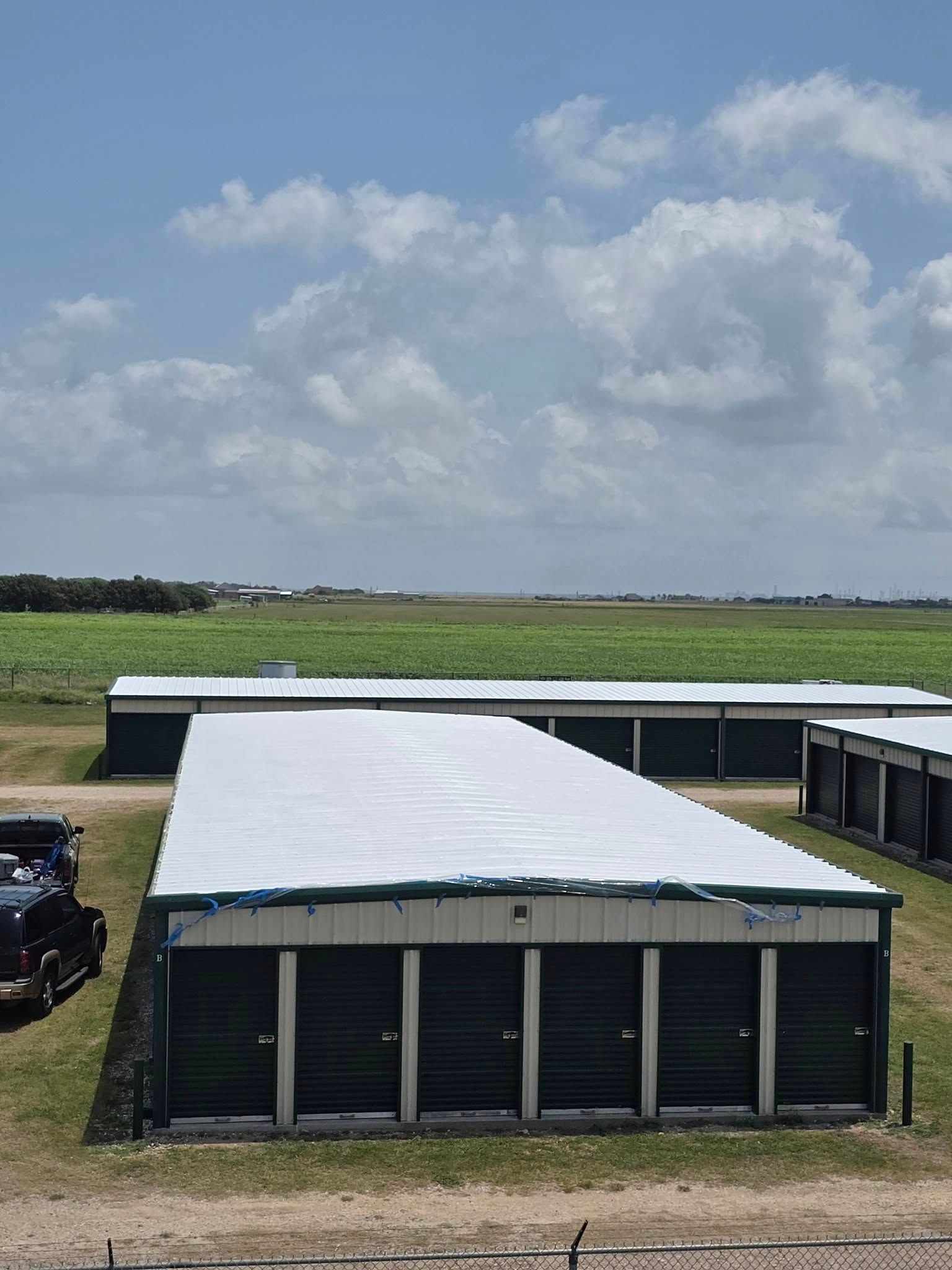 Low black storage buildings with white roofs in a grassy field under a cloudy sky