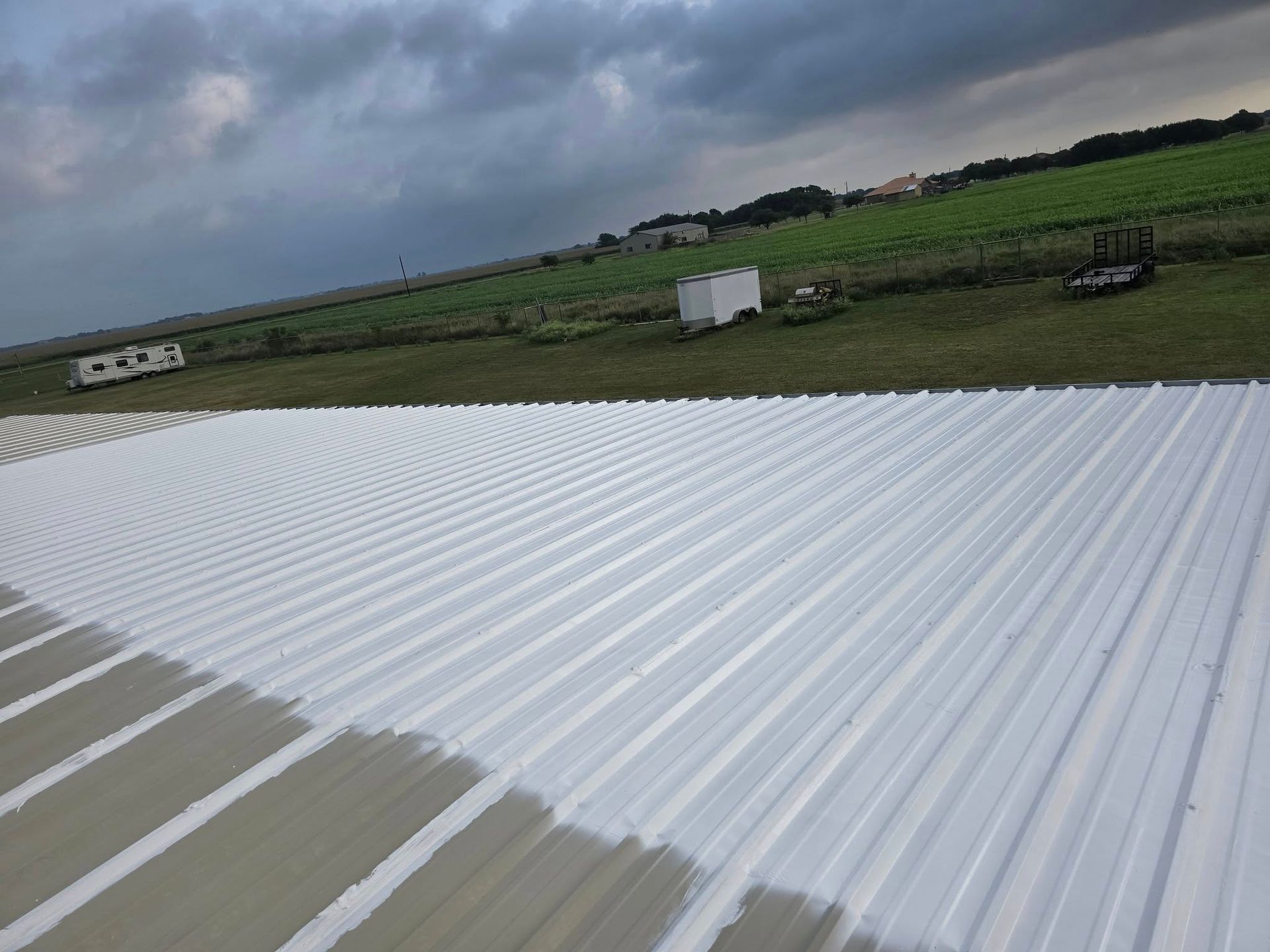 White corrugated roof in foreground with green fields and cloudy sky beyond