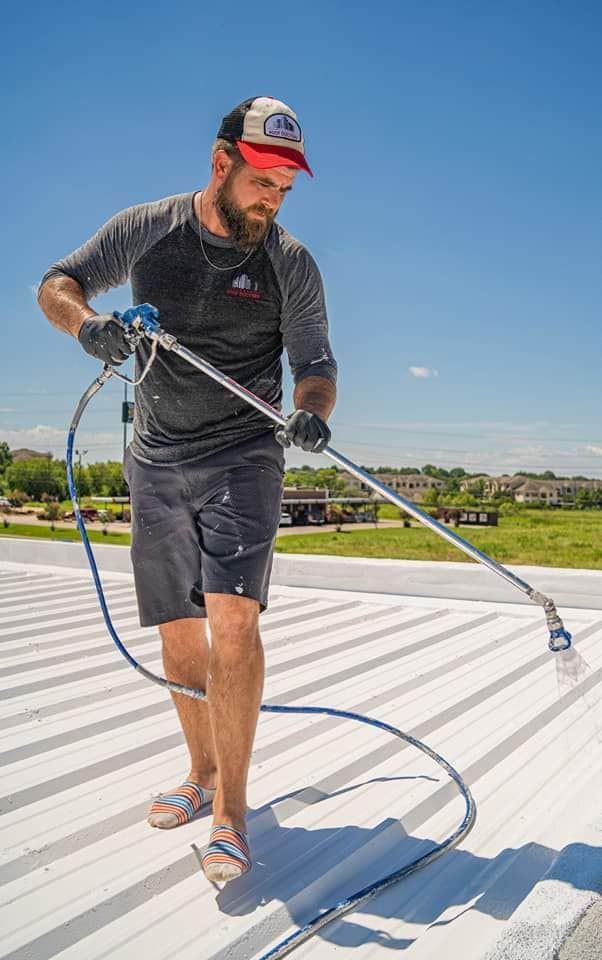 Worker power-washing a white rooftop under a blue sky, holding a hose wand.
