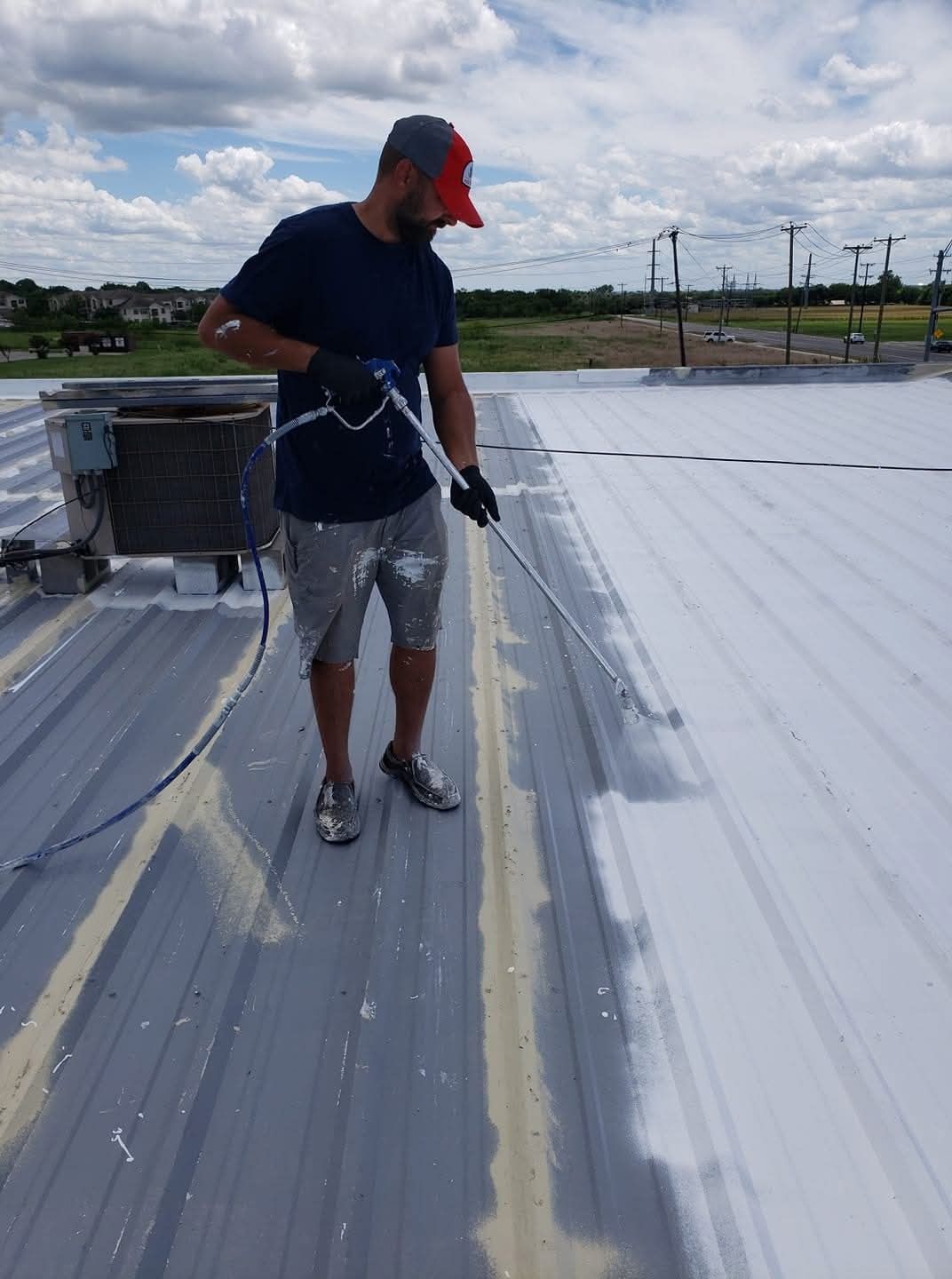 Worker applying white coating on a flat rooftop with a roller under a cloudy sky