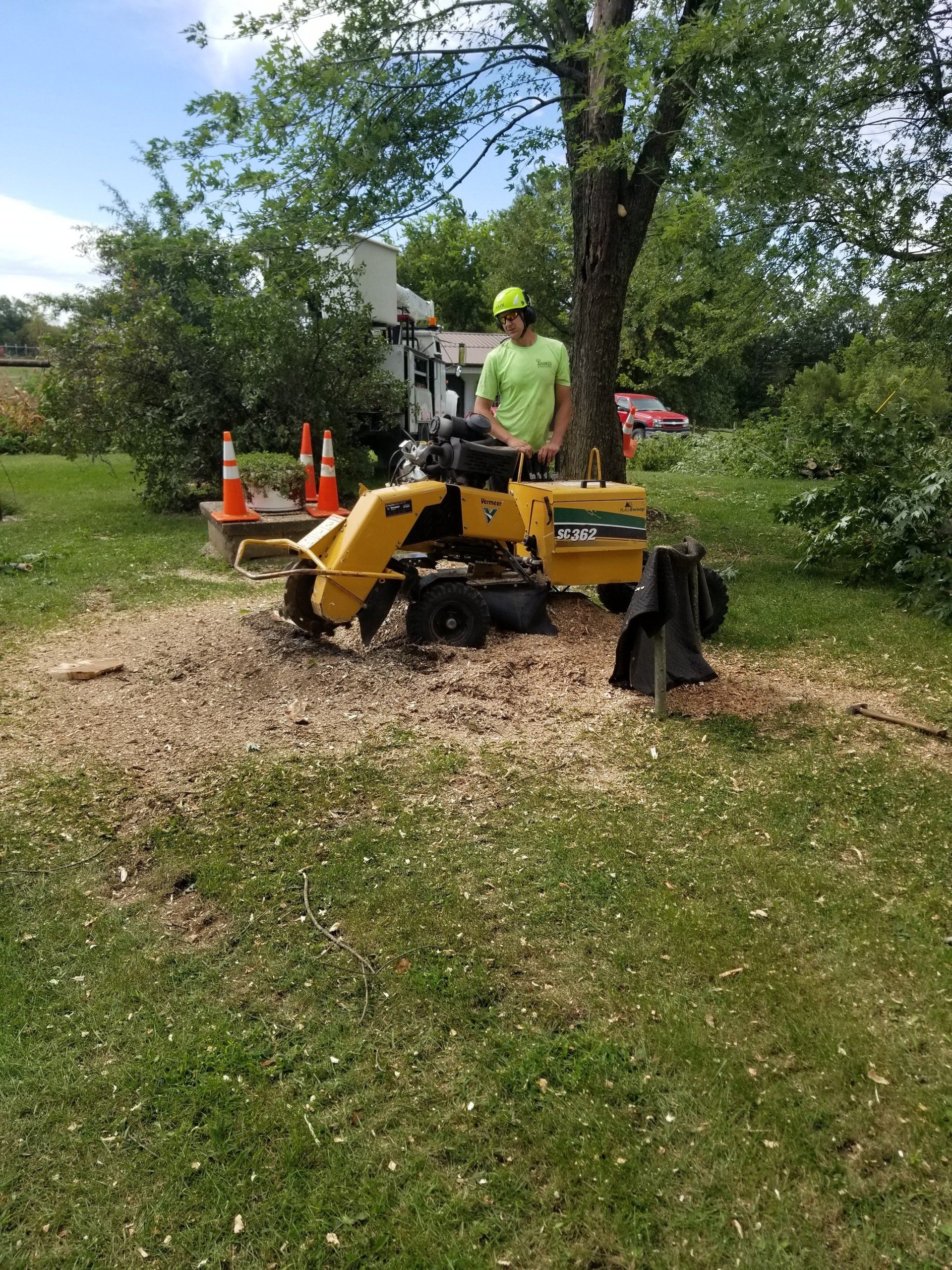 A man is standing next to a stump grinder in a yard.