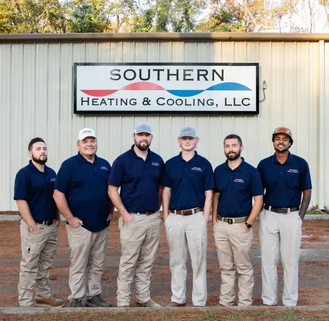 Group of seven employees in work uniforms, standing in front of Southern Heating & Cooling building.