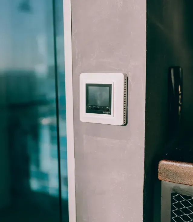 White thermostat with digital display mounted on a gray wall.