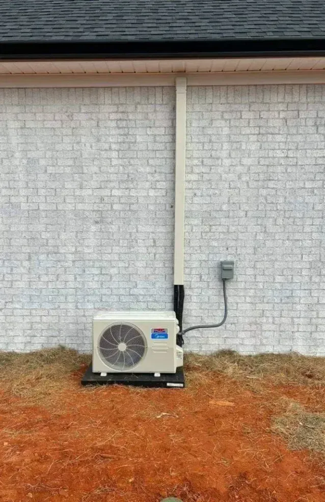 Outdoor air conditioning unit against a painted white brick wall. Electrical conduit and box are visible.