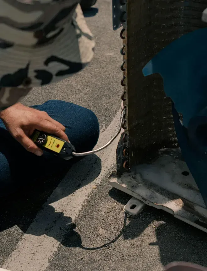 Person in jeans using a meter on an outdoor air conditioning unit.