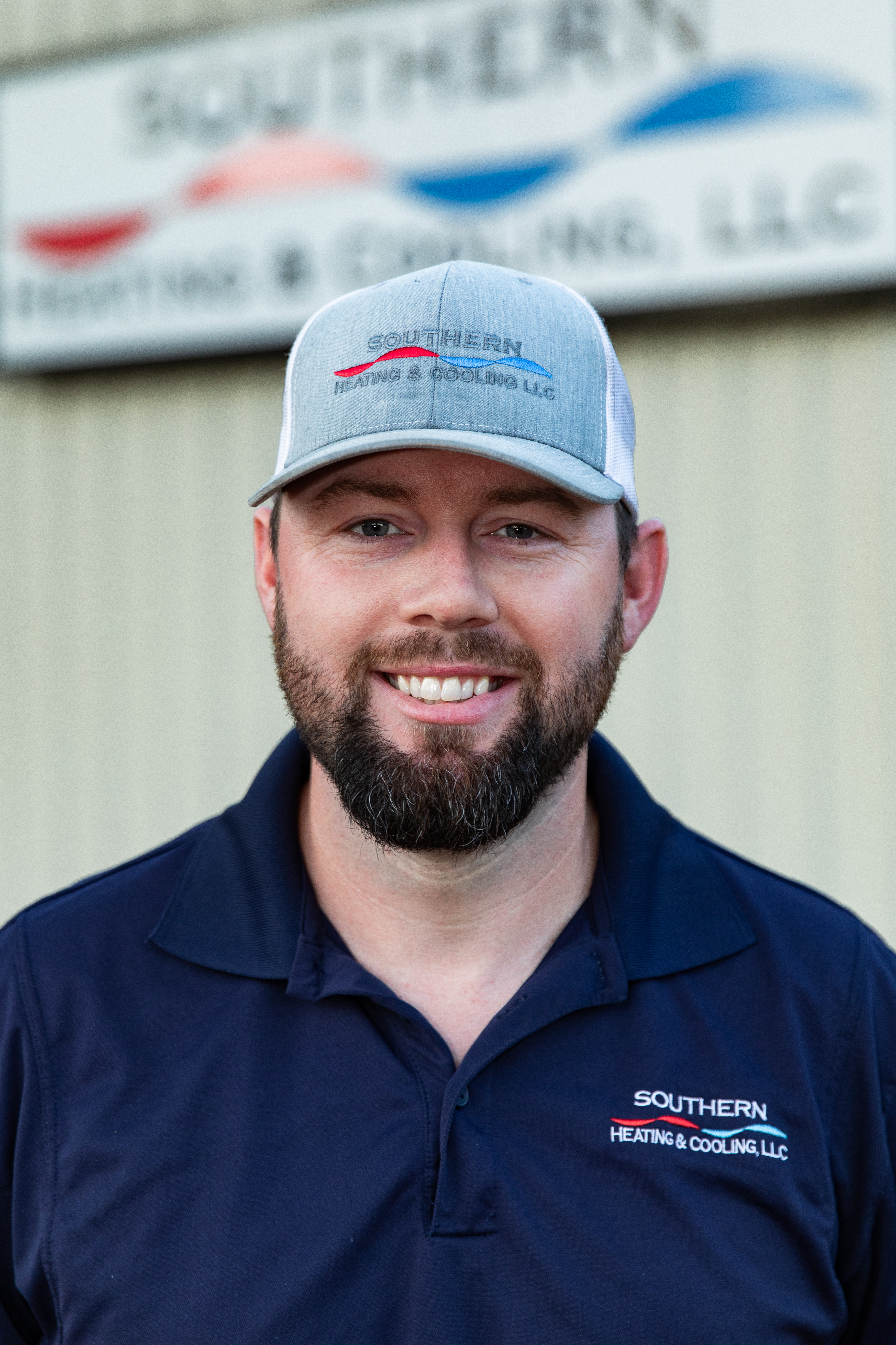 Man wearing Tempstat hat, smiling, seated at a desk, dark blue shirt, neutral wall background.