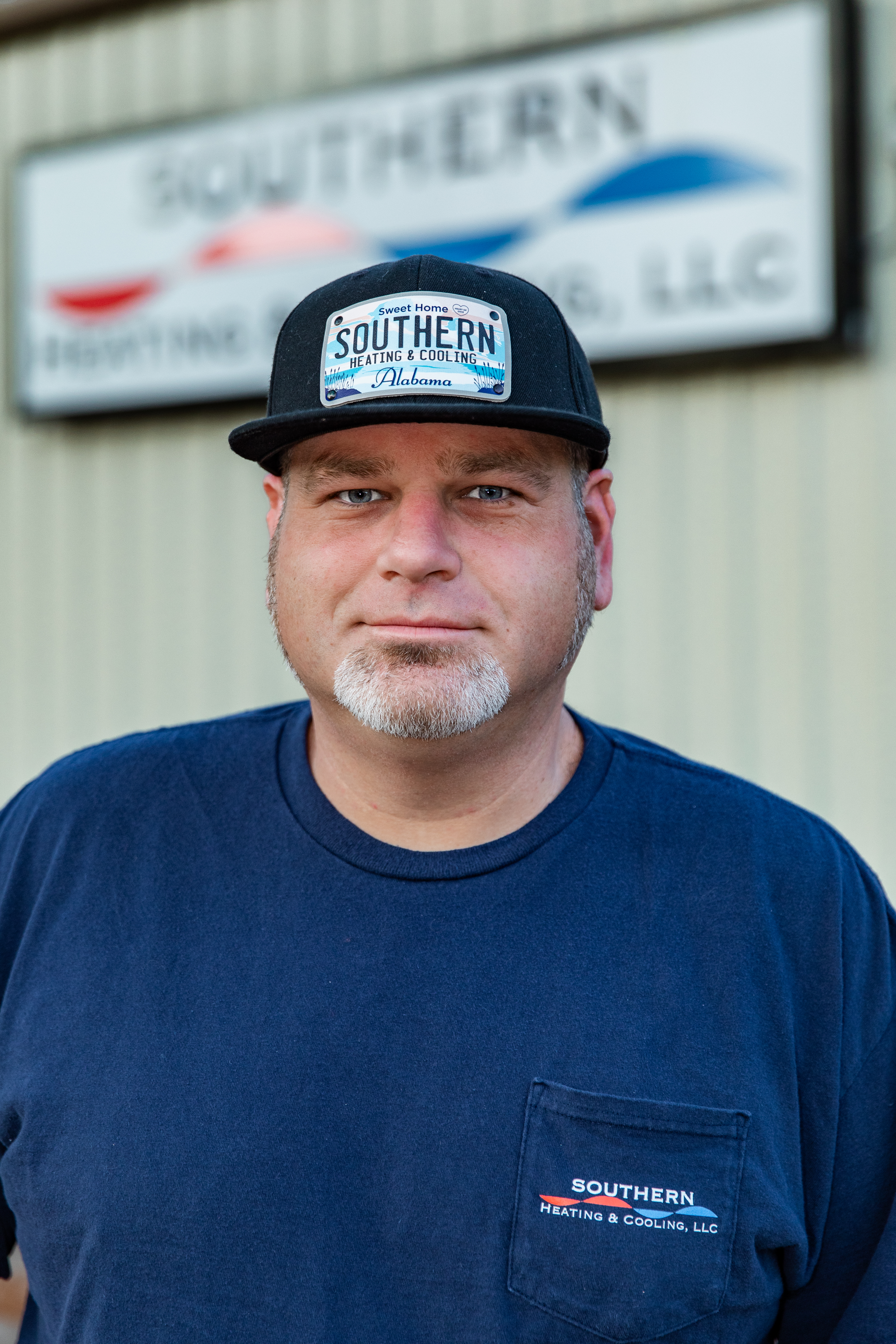 Man wearing gloves smiles while working at a table. Wooden wall backdrop.