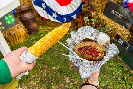 A person is holding a corn on the cob and a baked potato.