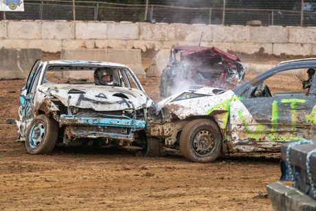 Two wrecked cars are racing on a dirt track.