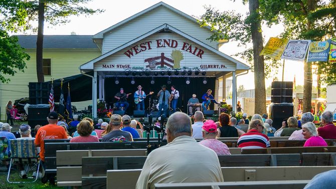 A group of people are sitting in front of a stage at the west end fair