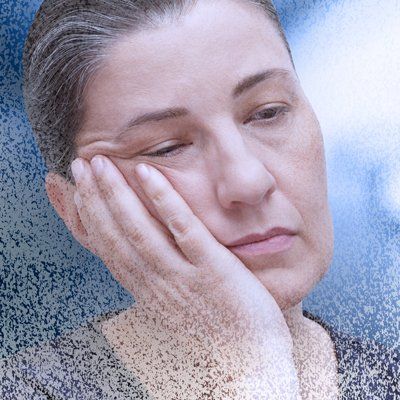 A woman with Adrenal Fatigue symptoms resting her face in her hand, looking pensive behind a frosted glass pane