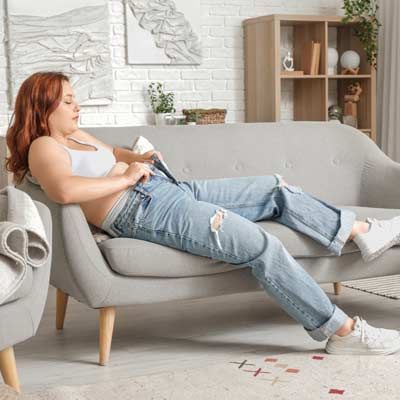Sudden and Unexplained Weight Gain is a Symptom of a Cortisol Imbalance A Woman with a cortisol imbalance reclining on a gray sofa, struggling with sudden weight gain
