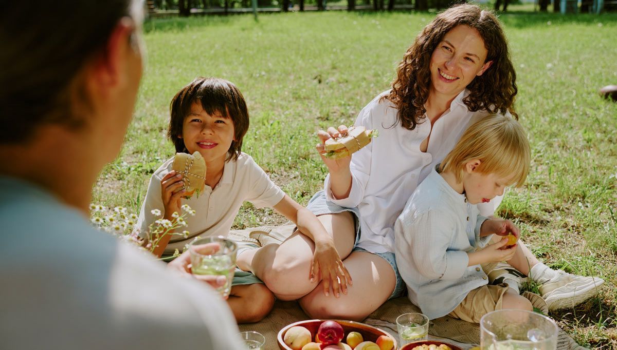 Family picnic on grass, with a woman practicing summer weight management