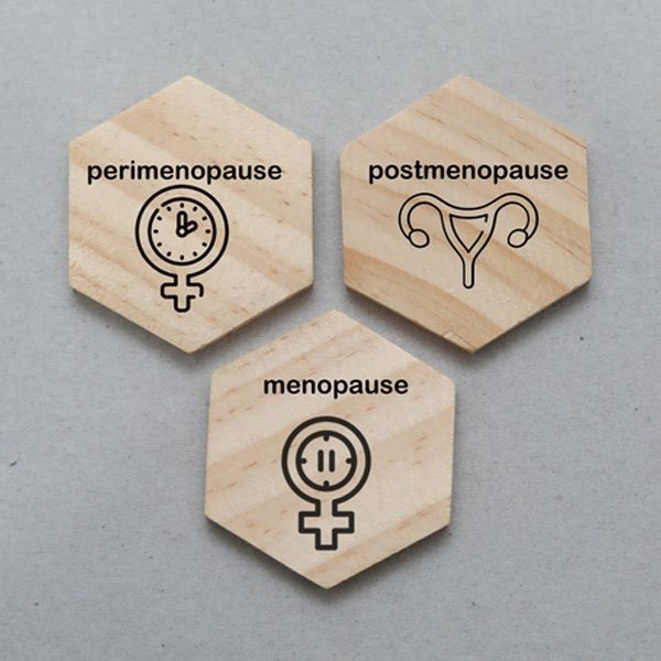 Three wooden hexagon tiles labeled perimenopause, postmenopause, and menopause with female symbols.