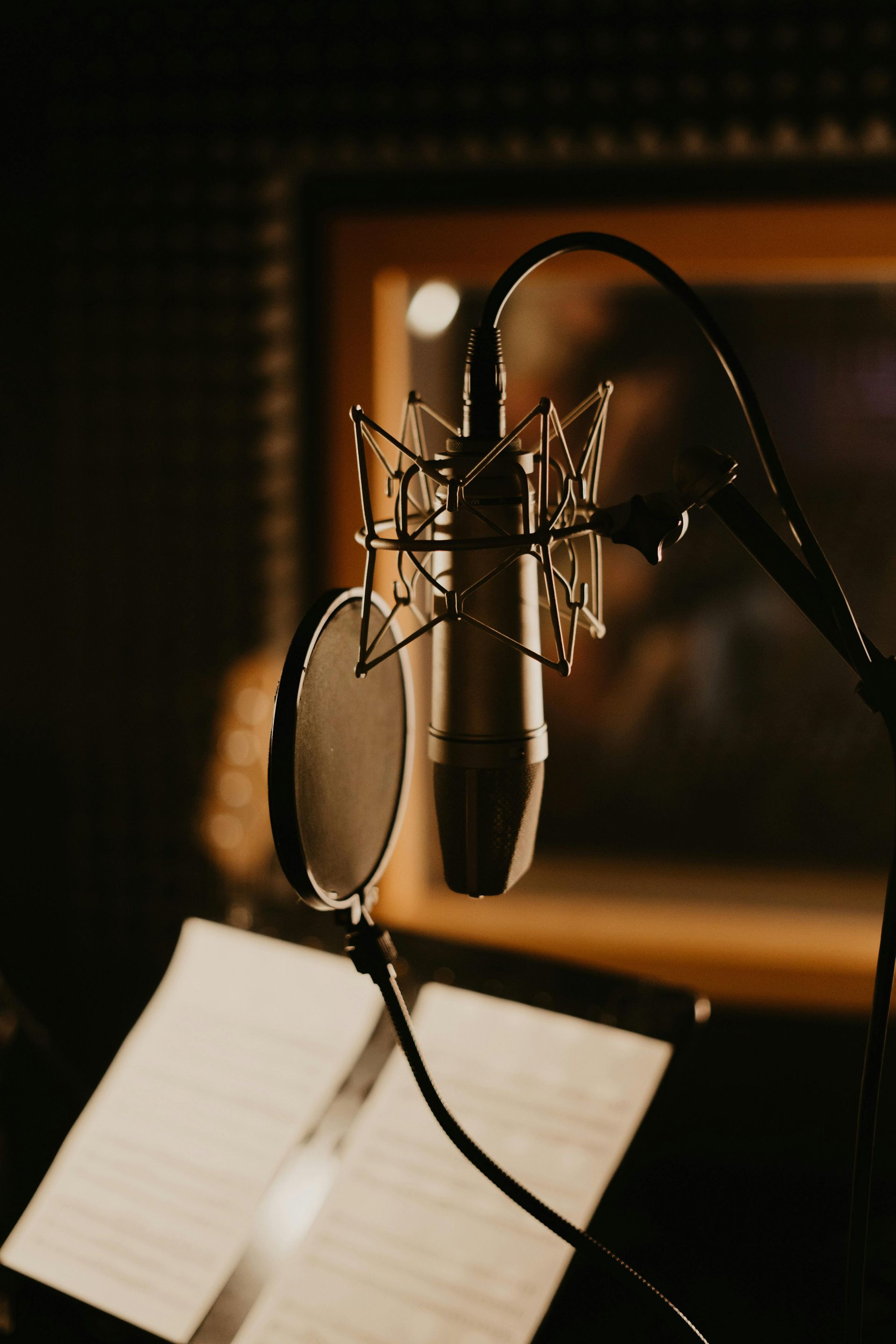 Studio microphone with pop filter and sheet music in a dim recording booth