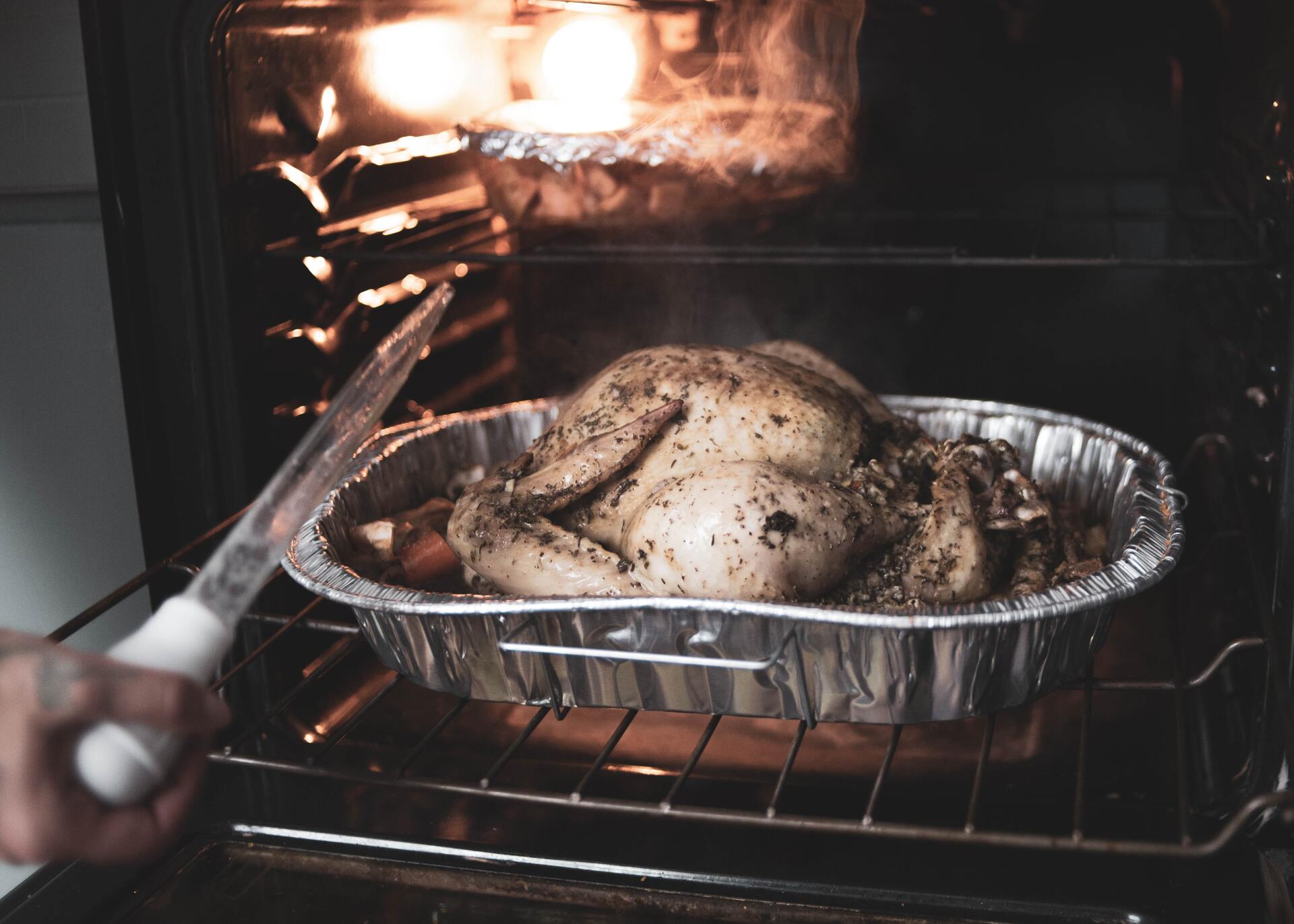 A person is taking a roasted chicken out of the oven.