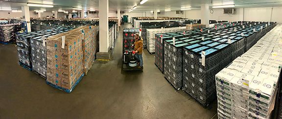Large storage room with numerous rows of egg crates stacked high, with a worker operating forklift in the background.