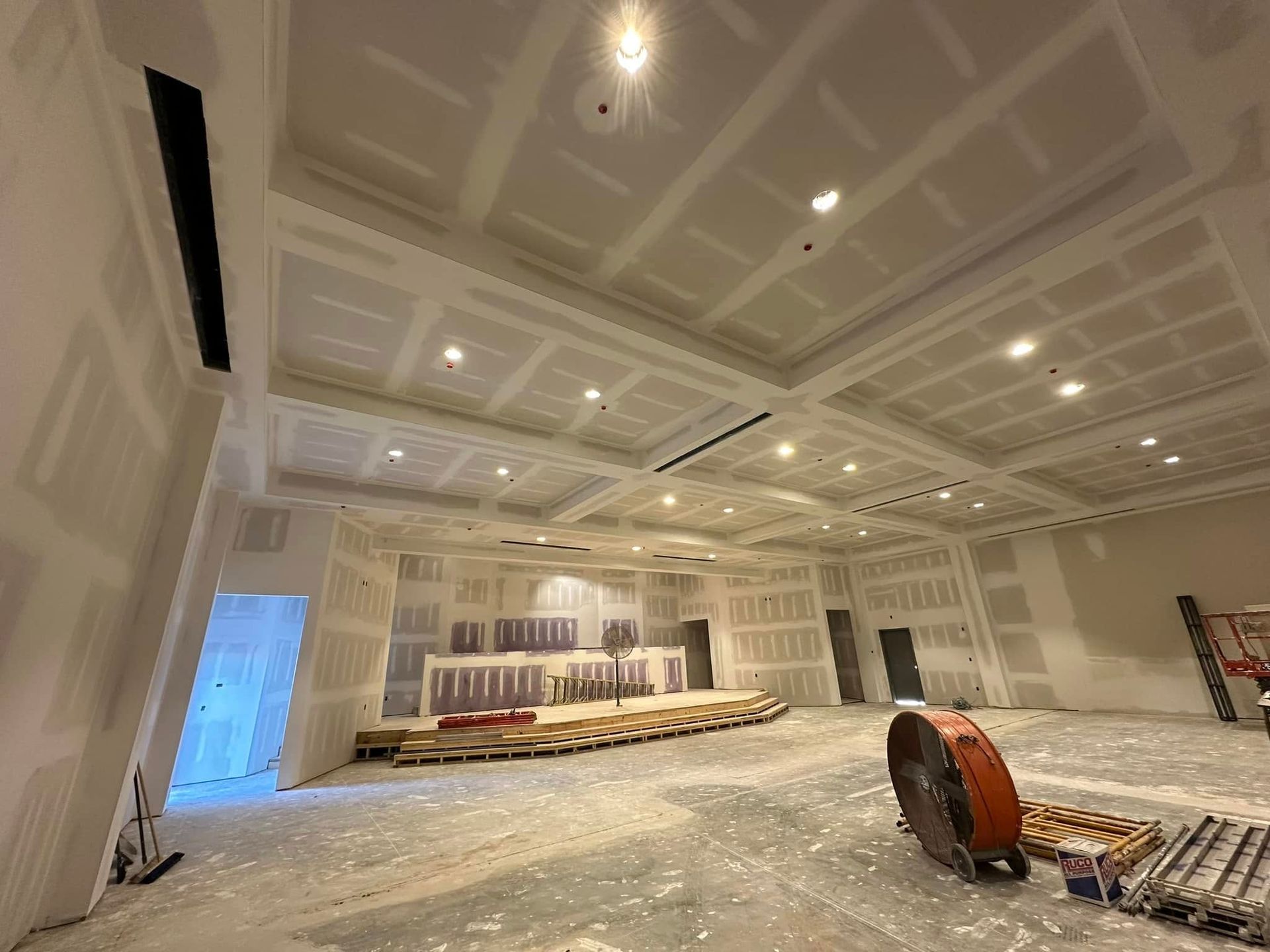 A large room with a ceiling that is being built and a fan on the floor.