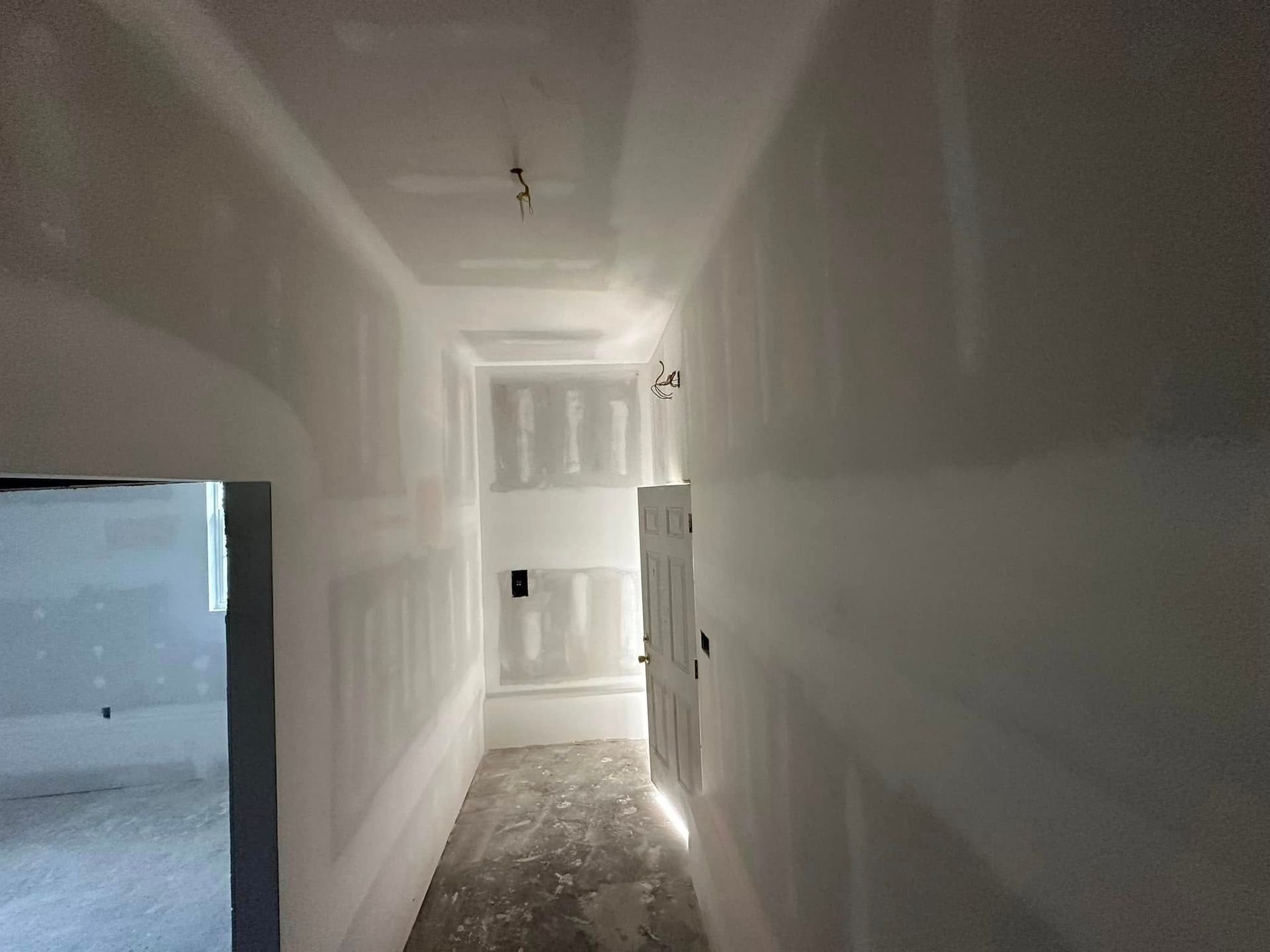 A long hallway with drywall on the walls and a door.