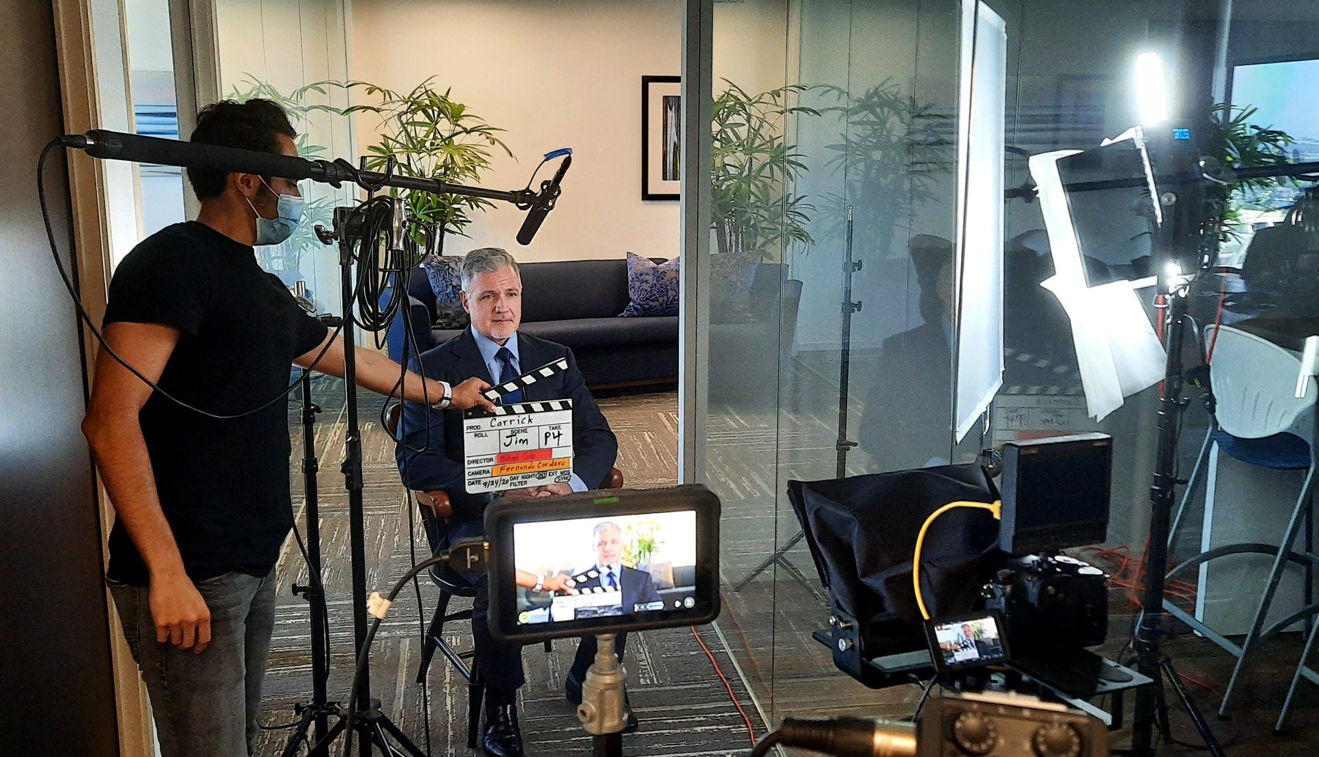 A man sitting with camera equipment around him and a PA holding the film slate